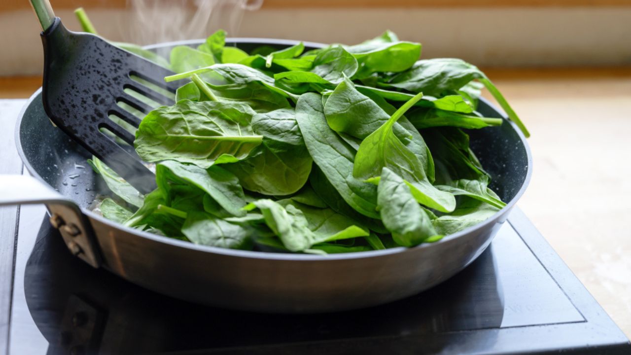 Frying fresh spinach in a pan on the stove, healthy cooking at home concept, selected focus, narrow depth of field