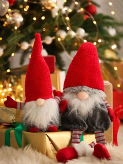 Adorable Christmas gnomes sitting on top of wrapped gifts in front of the tree.