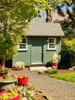 A green colored garden shed surrounded by flower pots.