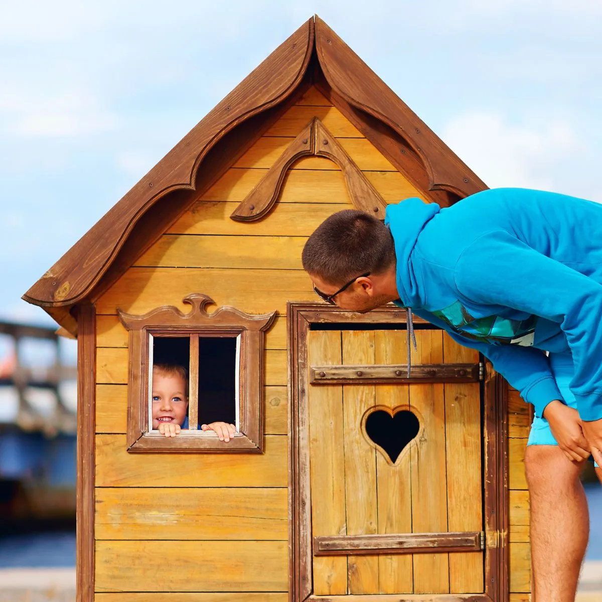 Man playing with kid inside smal wooden shed playhouse. 