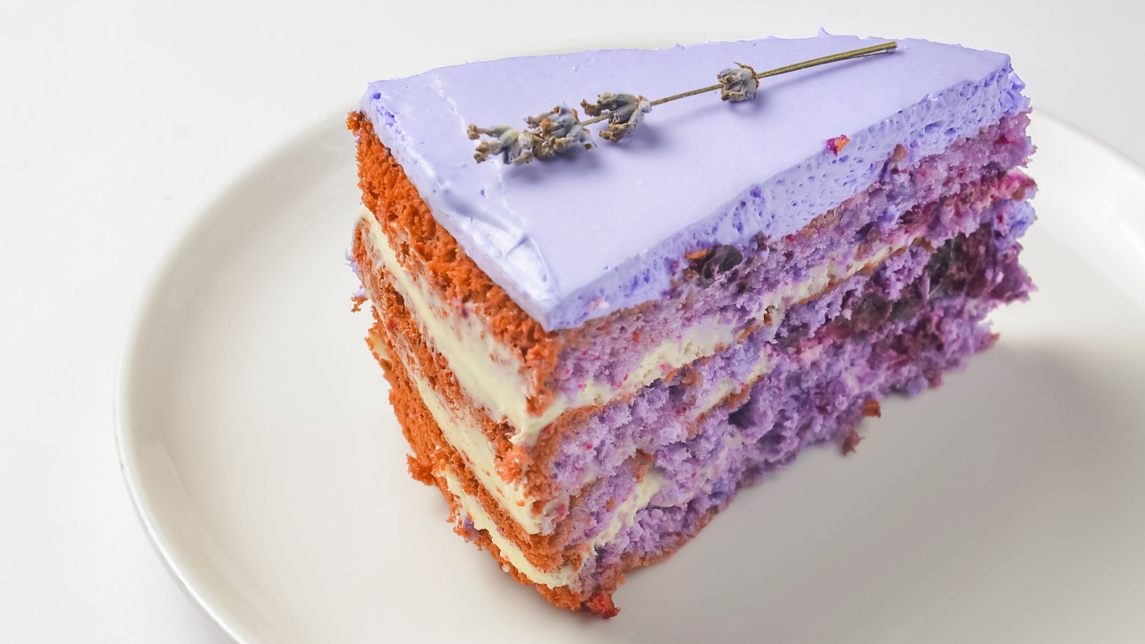 Cut lavander cake on a white plate. A piece of purple violet cake with lavander and berries served on a white plate over white background. Delicious sweet dessert for tea time.