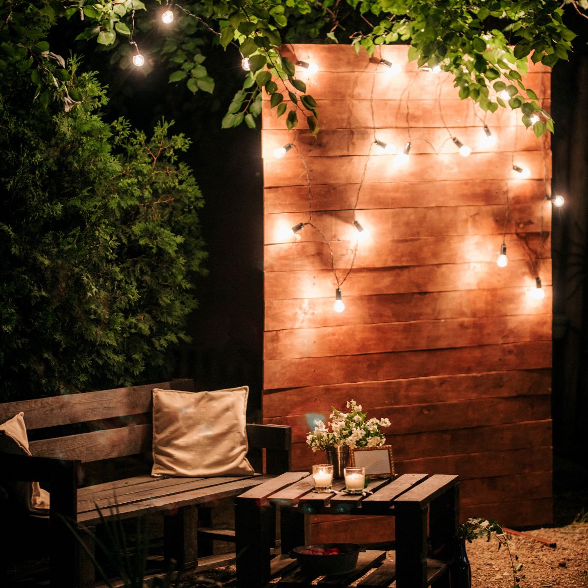 A bench and wooden table with a lit wooden backdrop.