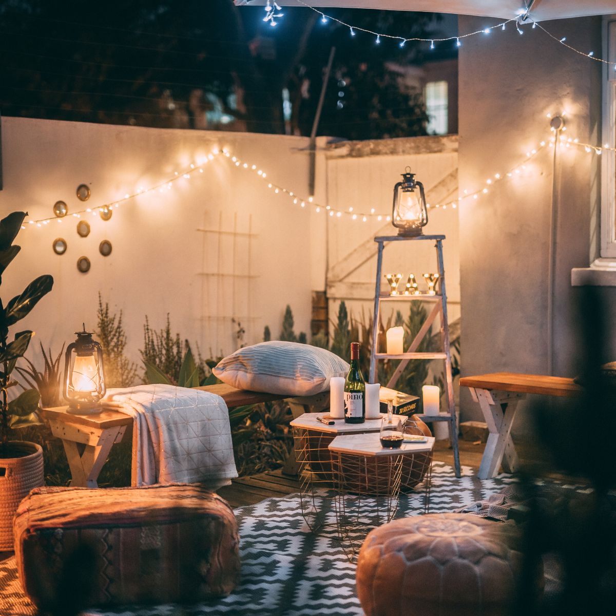 A very homey spot in the backyard, set up with a few sitting areas, a blanket, and lots of lighting. 