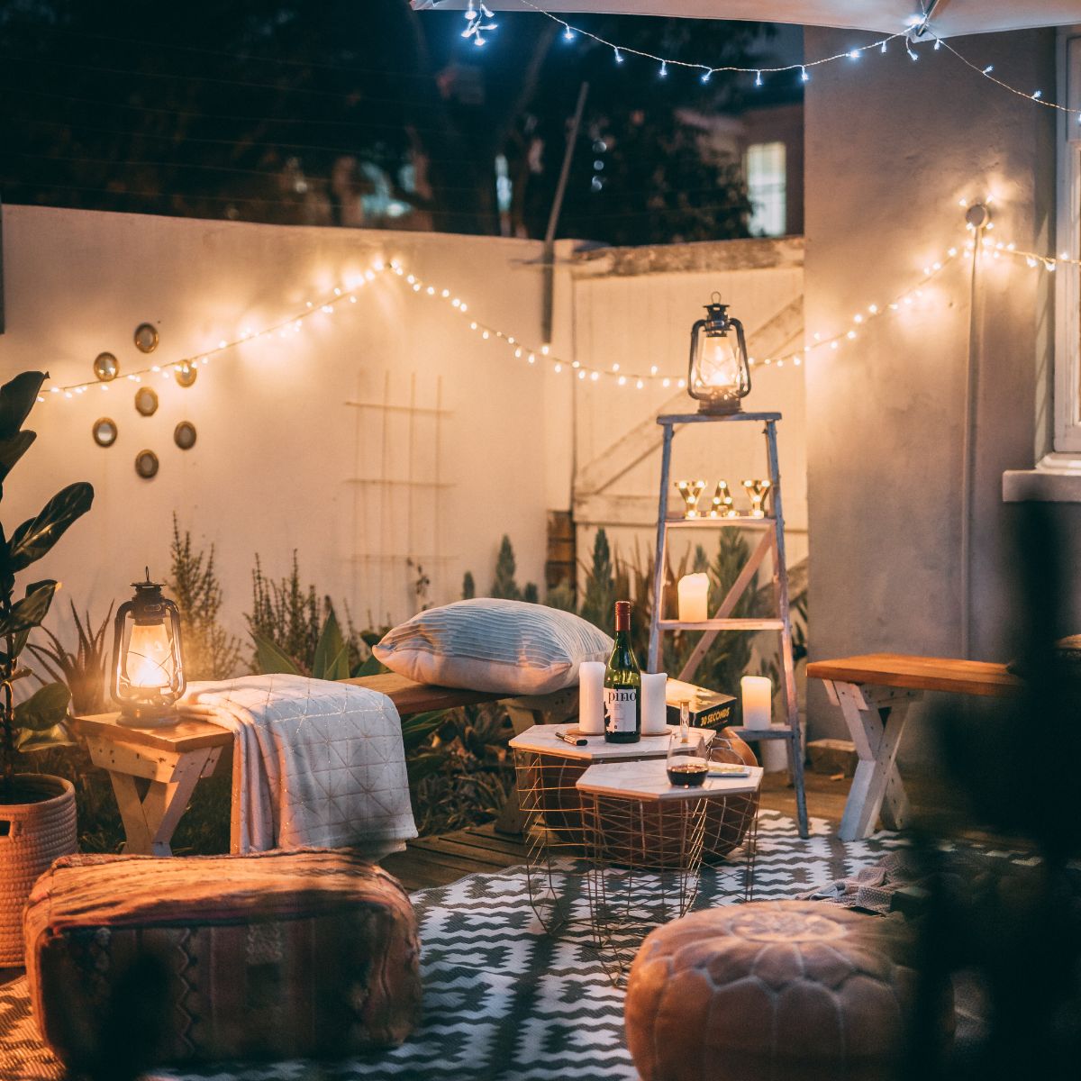 A very homey spot in the backyard, set up with a few sitting areas, a blanket, and lots of lighting.