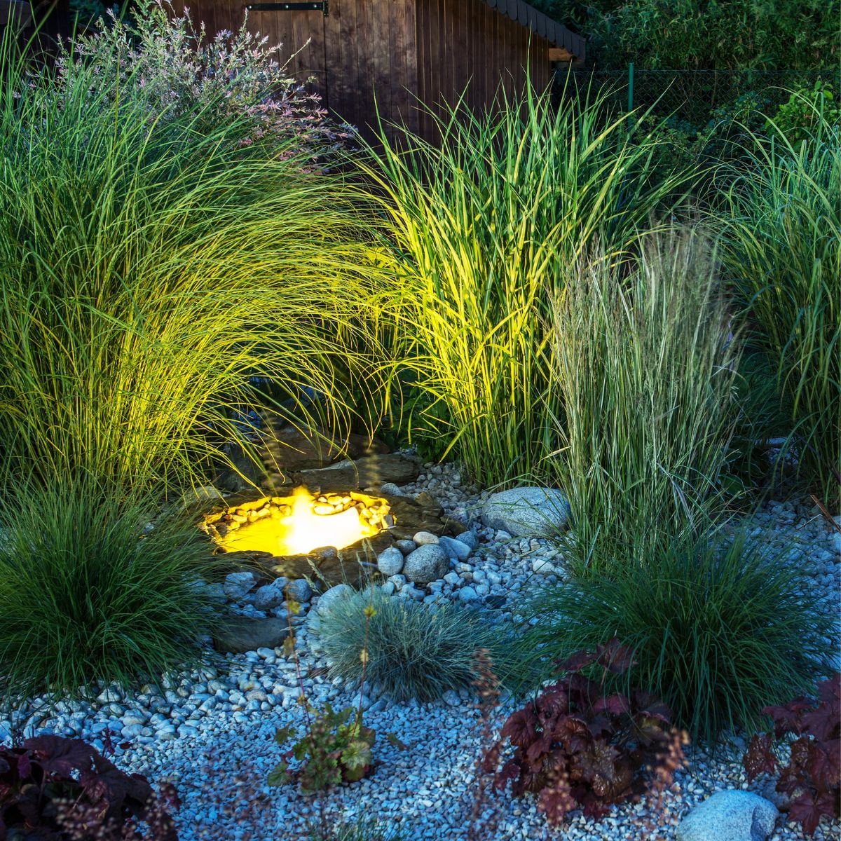 A rock and grass garden surrounds a soft glow-lit pond.