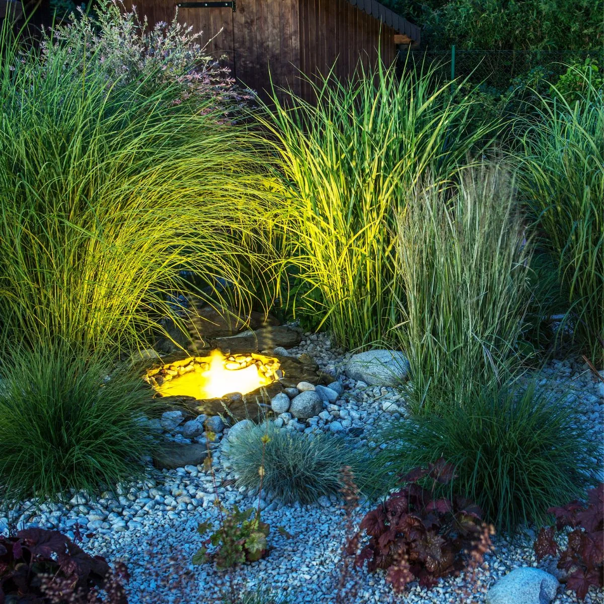 A rock and grass garden surrounds a soft glow-lit pond. 