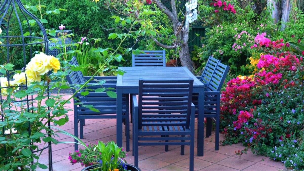 Blue table and chairs in a small backyard, surrounded by red and yellow roses. 