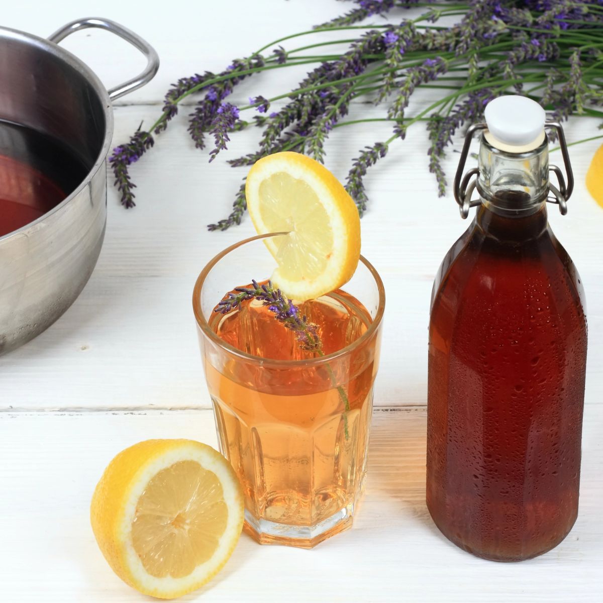 A bottle of lavender syrup next to a glass of tea and half of a lemon.
