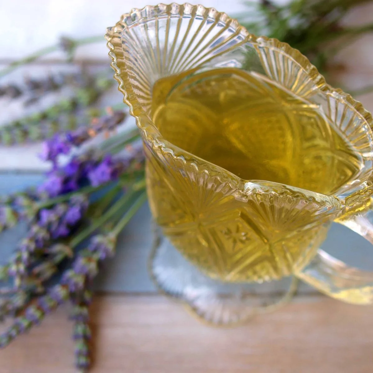 a glass of lavender syrup with some fresh lavender behind it.