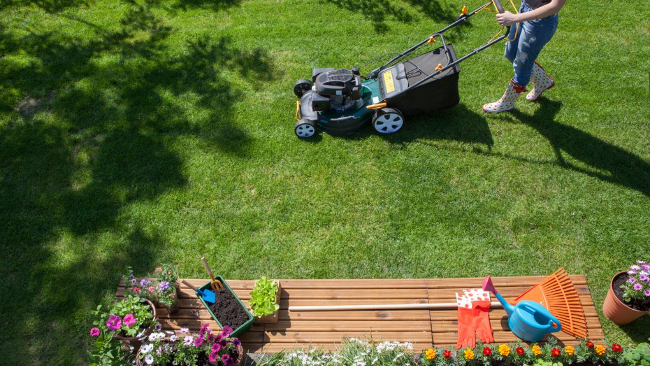 Woman wearing wellington boots mowing grass with lawn mower in the garden, gardening tools concept