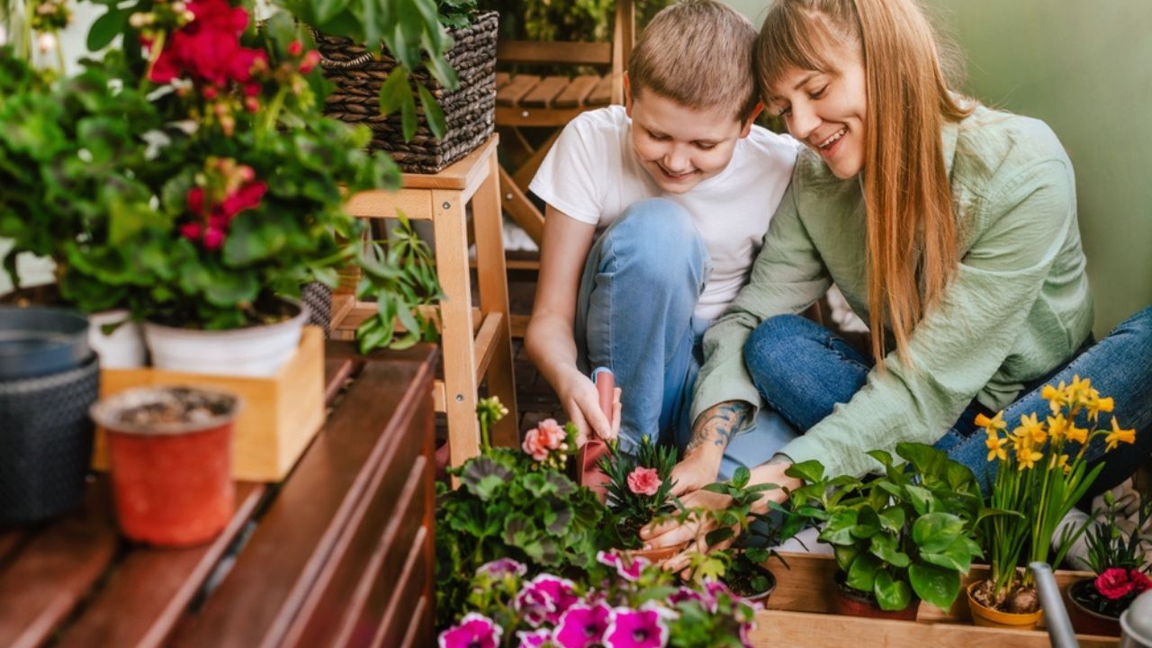 Happy mother and son planting flowers in home garden. Cheerful mom and boy spending time together, gardening at city balcony.