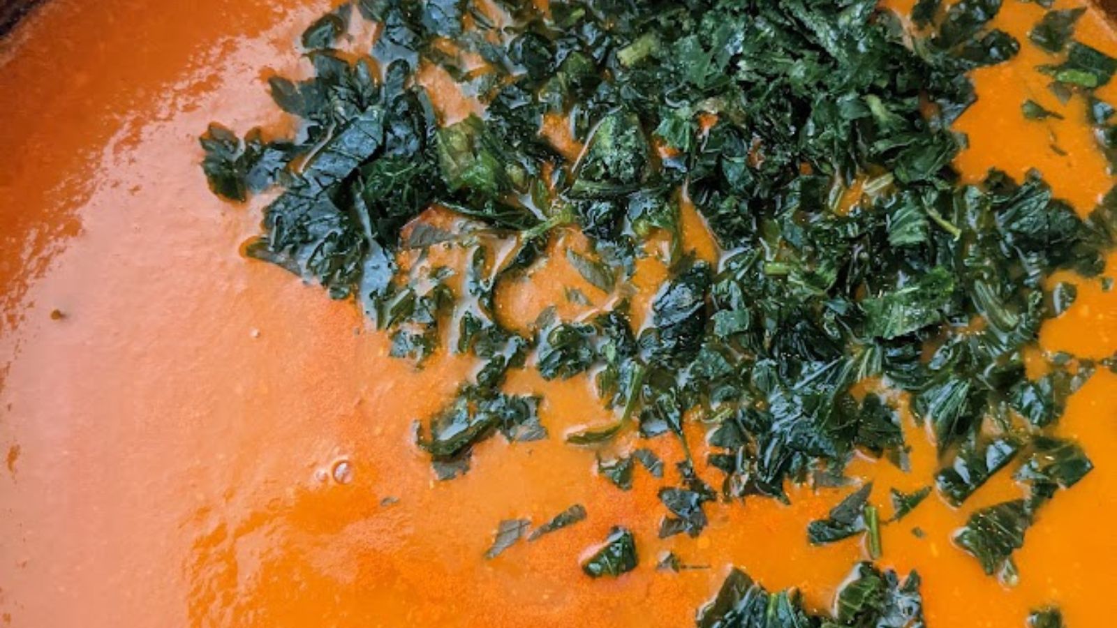 a pot of creamy tomato soup with chopped celery leaves on top.