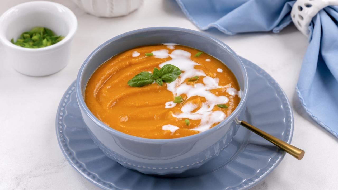 Sweet potato pumpkin vegetable soup with coconut cream and basil leaves on on white stone background.