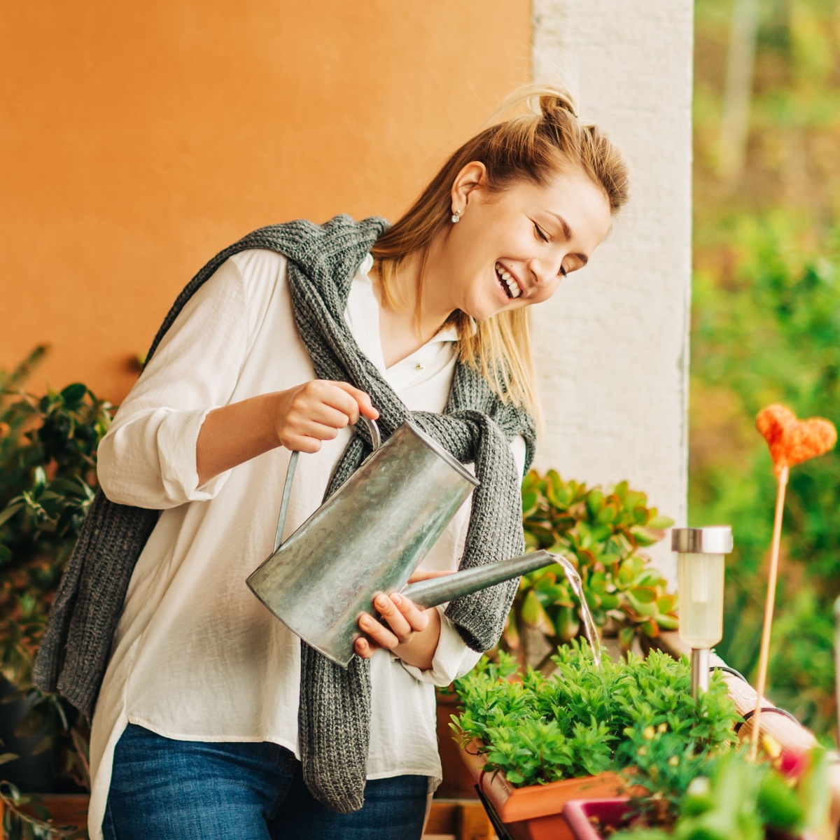 Portrait of beautiful woman watering green plants on the balcony, small cozy garden in apartment