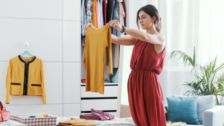 Elegant woman in her bedroom, she is decluttering her wardrobe and choosing clothes