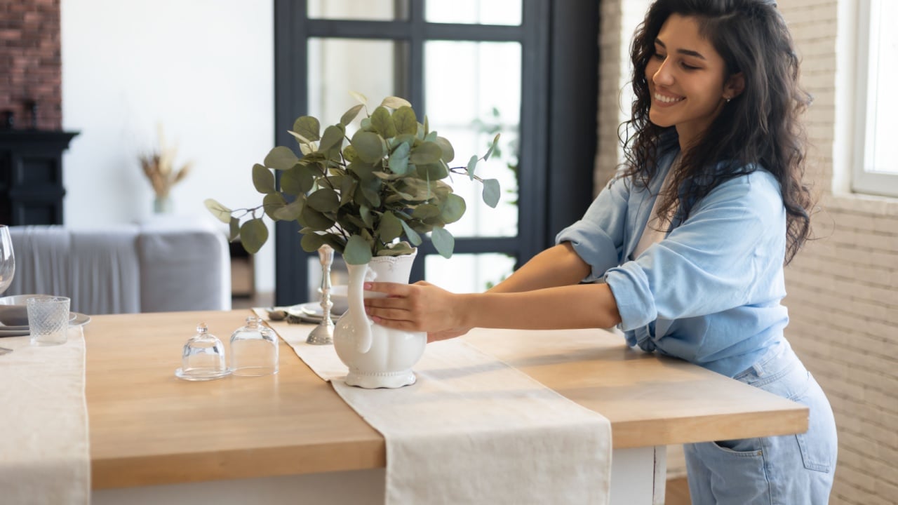 Modern home interior design, Scandinavian style concept. Beautiful young brunette woman arranging plants in vase