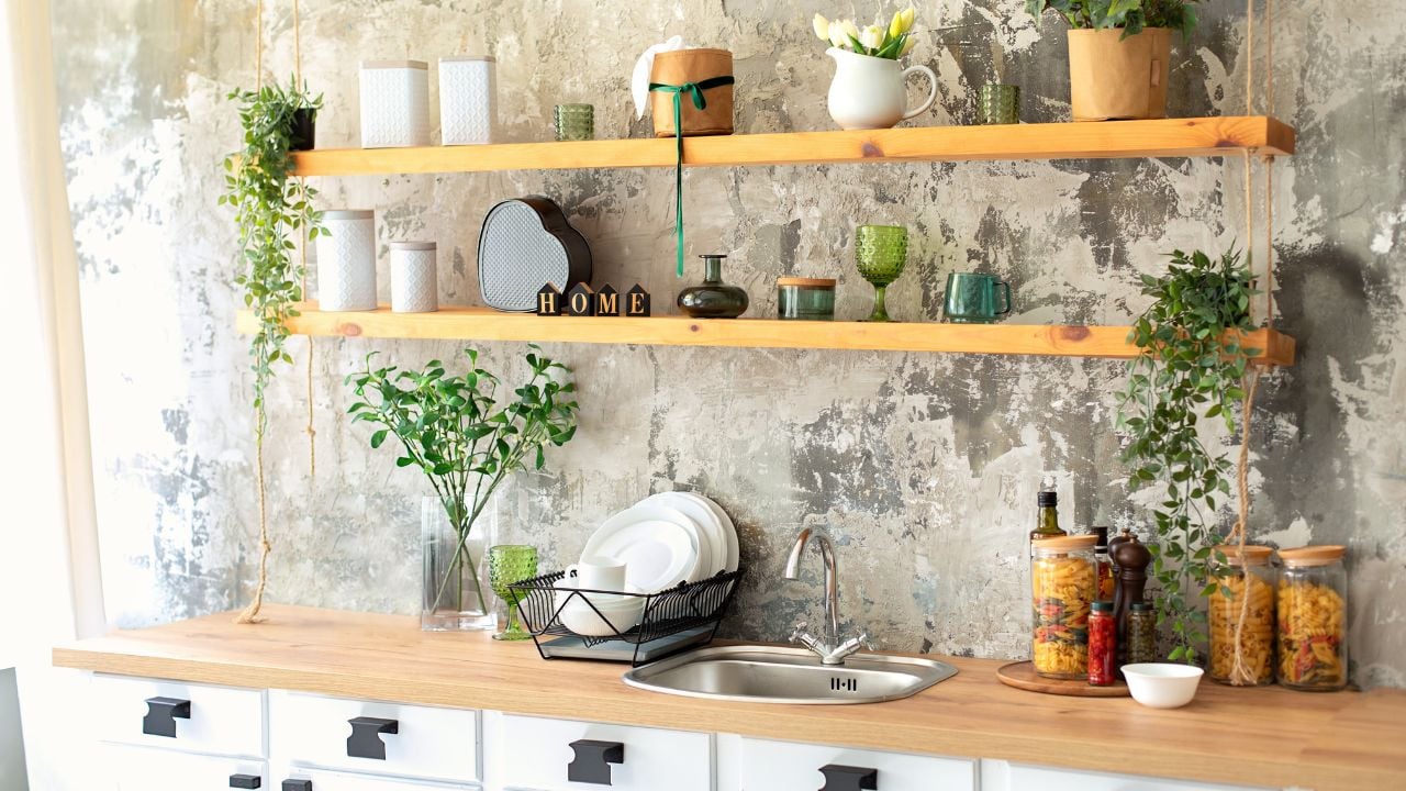 Stylish scandi white cuisine interior decor. Ceramic plates, green plants in pots, dishes and cozy decor on wooden shelves. Kitchen wooden shelves with various cookware. Open shelves in the kitchen.
