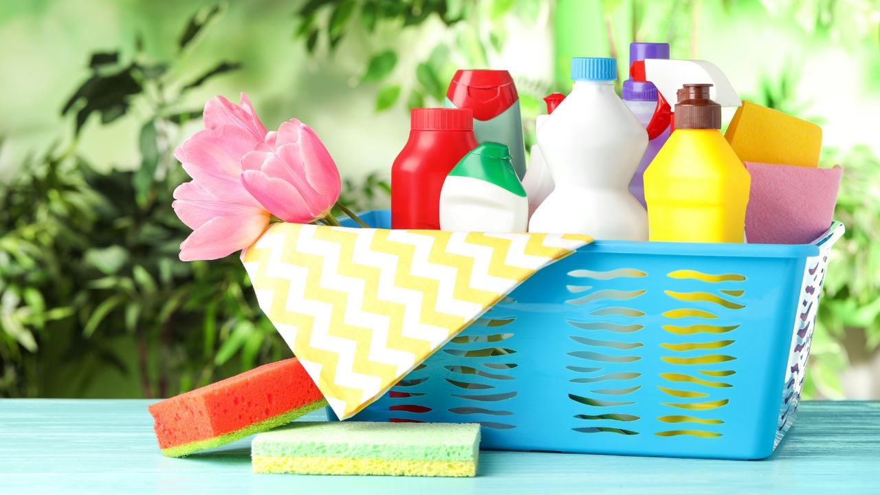 Plastic basket with spring flowers and cleaning supplies on light blue wooden table