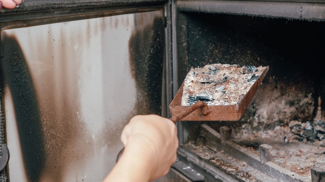 Fireplace cleaning. A woman's hand holds a shovel with ash in a burnt-out fireplace.