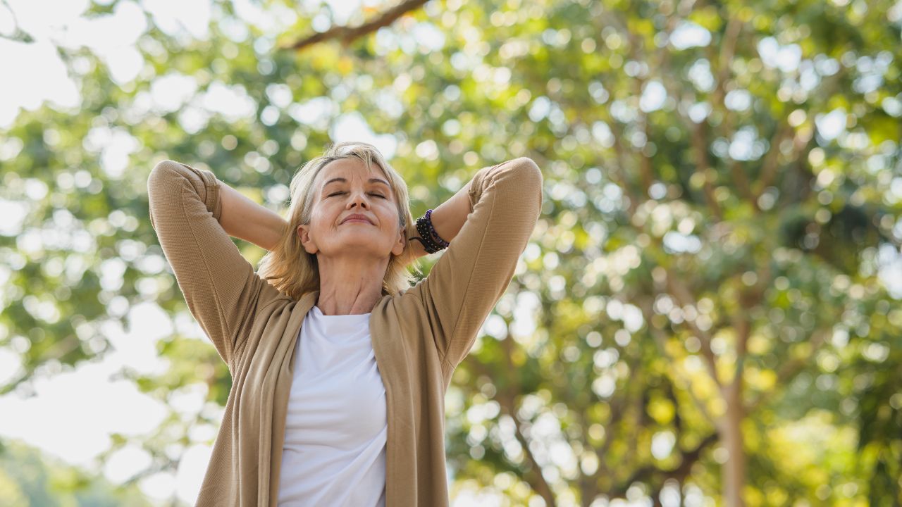 Portrait photo of happy senior Caucasian woman relaxing and breathing fresh air with sunlight in outdoors park. Elderly woman enjoying a day in the park on summer. Healthcare lifestyle and wellness