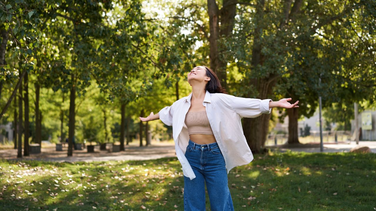 Carefree asian girl dancing, feeling happiness and joy, enjoying the sun on summer day, walking in park with green trees.