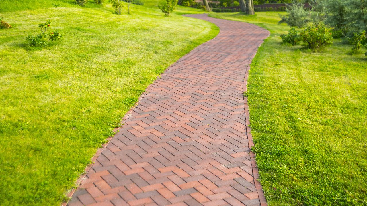 Brown stone pathway in the park background. Brown concrete pathway with green grass lawn in the park backdrop