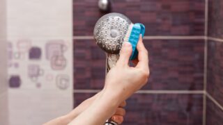 Woman cleaning an calcified shower head in domestic bathroom with small brush.