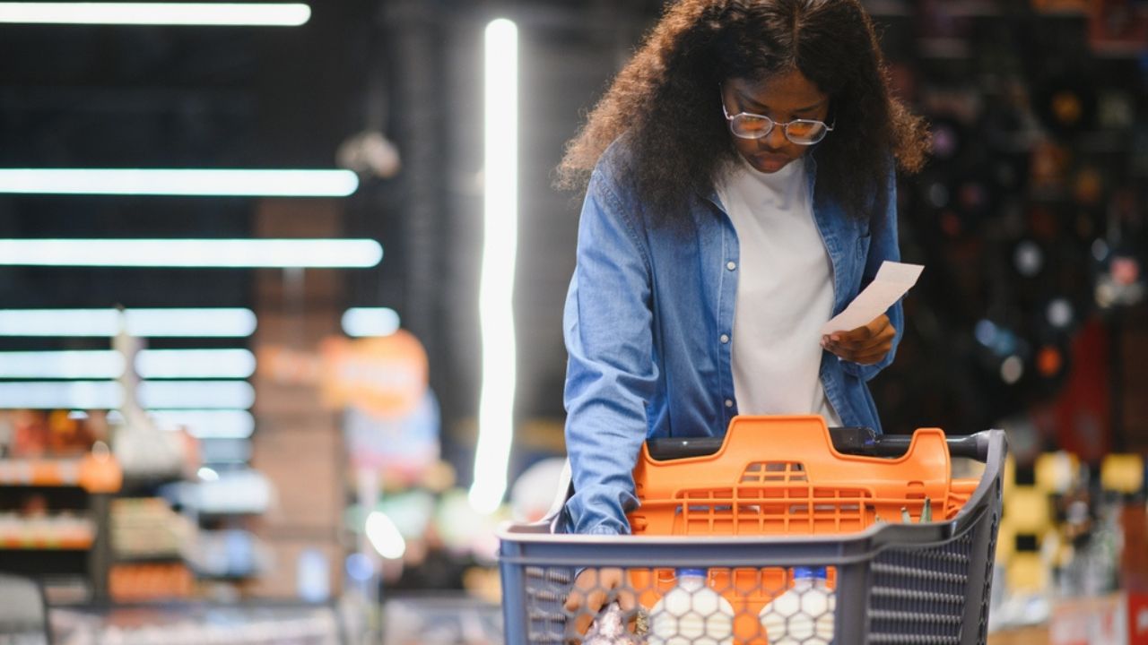 African American Female Customer Posing With Shop Cart Buying Food Products In Supermarket, Smiling Looking At Camera. Black Woman Choosing Groceries In Store Concept