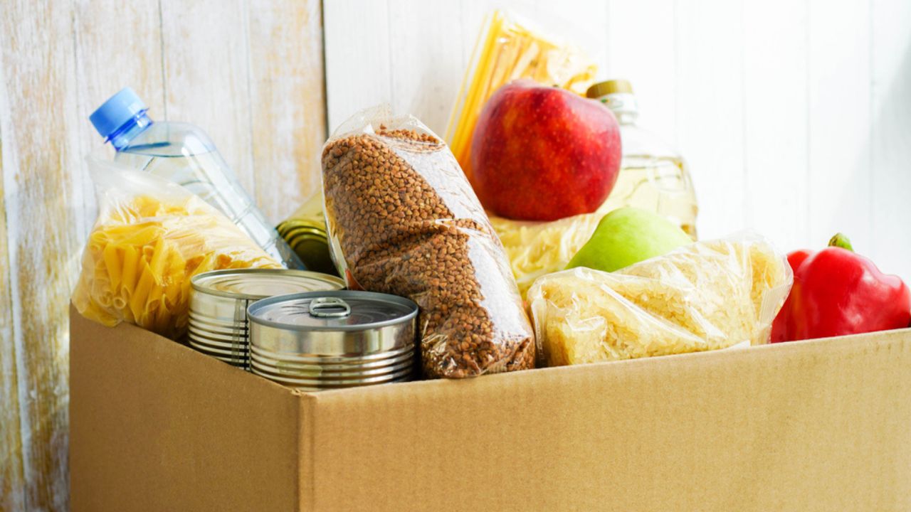 Donation box with various food. Open cardboard box with butter, canned goods, cereals and fruits.