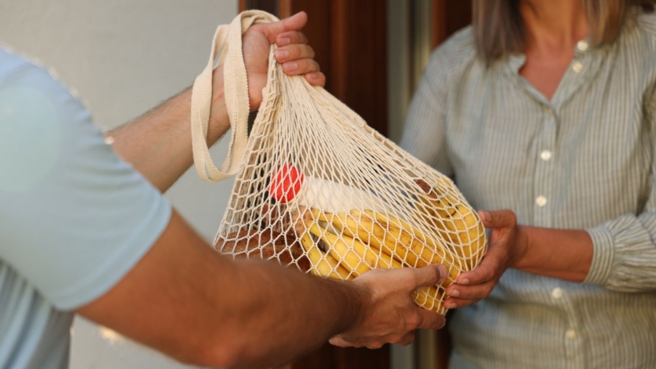 Helping neighbours. Man with net bag of products visiting senior woman outdoors, closeup