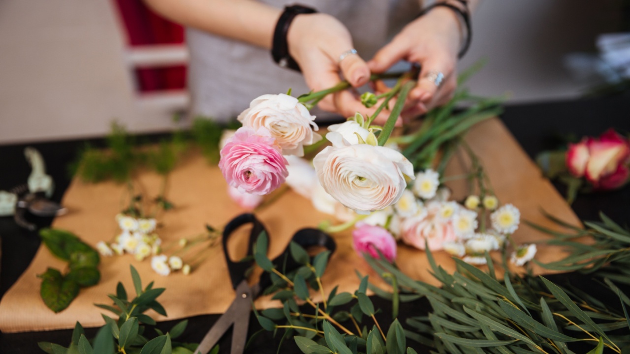 Closeup of hands of young woman florist creating bouquet of pink roses on the table