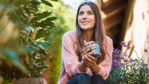 woman enjoying coffee in her garden with purple flowers