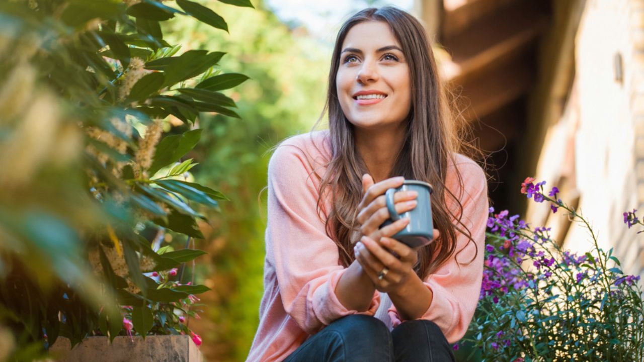 woman enjoying coffee in her garden with purple flowers