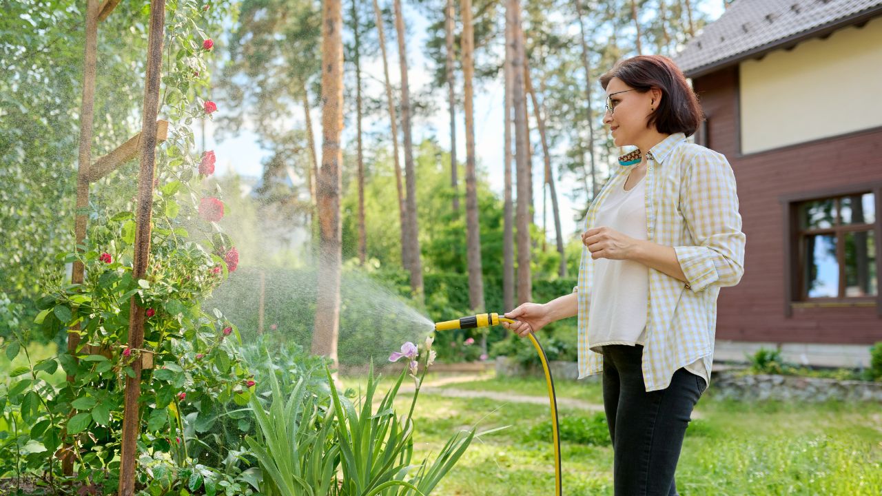 woman in her yard watering flowers with a hose sprayer