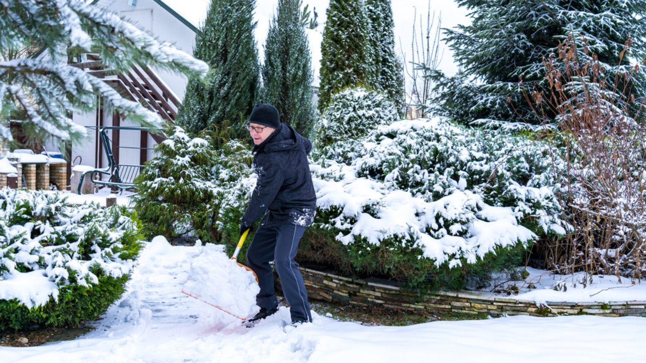 A 61-year-old elderly Caucasian man enthusiastically throws snow in the yard with an orange shovel. Healthy lifestyle concept in old age