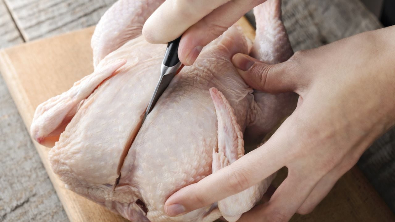 A girl knives a raw chicken into pieces on a cutting board.