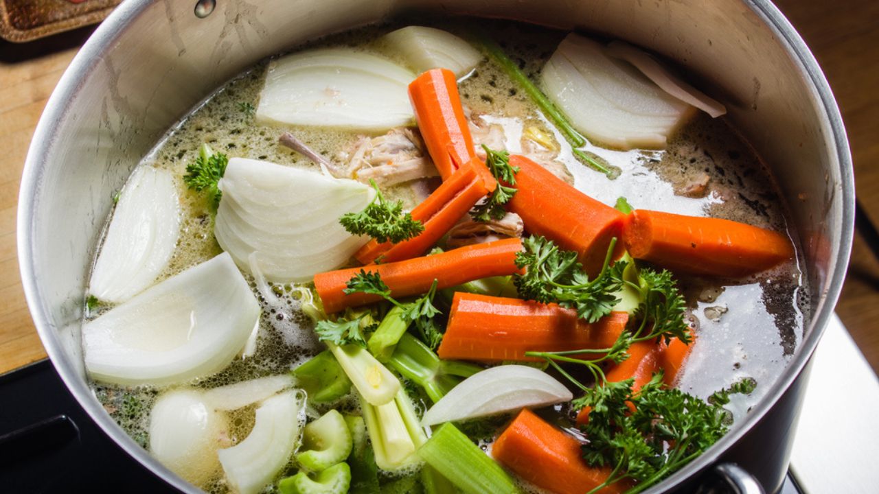 A large stock pot on a stove with vegetables cut for making soup