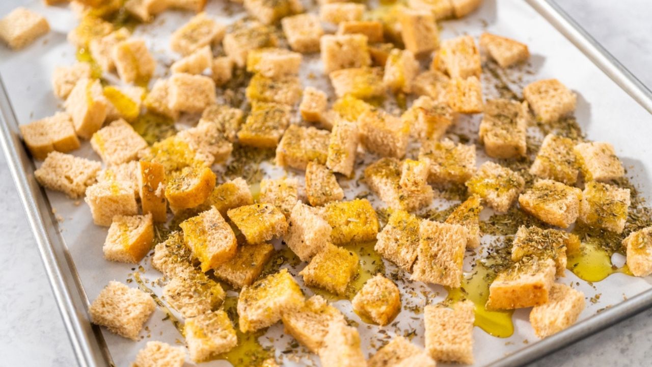Baking croutons seasoned with olive oil and spiced on a baking sheet lined with parchment paper.