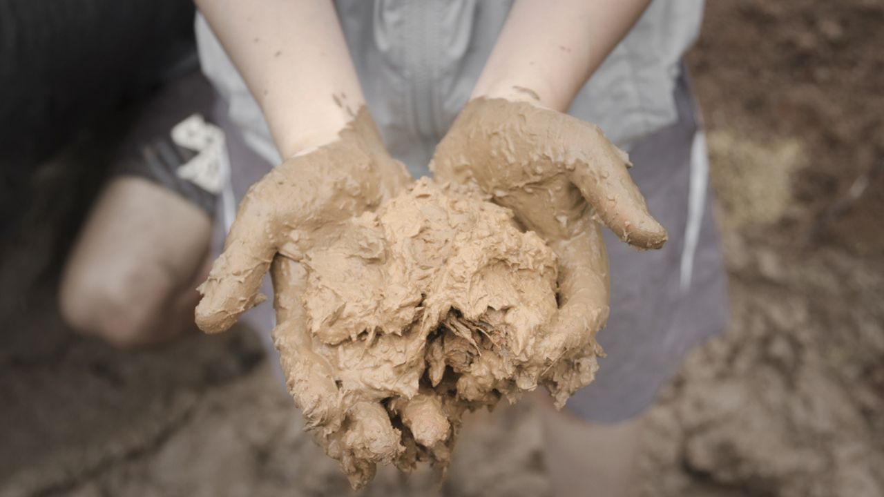 Full of mud, clay on young woman hands with lower body standing in mud pool background. Preparing mud, clay to make brick clay for built a clay house