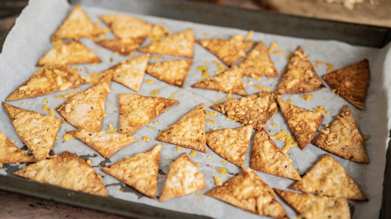 Process of cooking cheese Tortilla chips with olive oil on baking sheet after oven, homemade salty savory pastry snack in the kitchen. Selective focus with copy space.