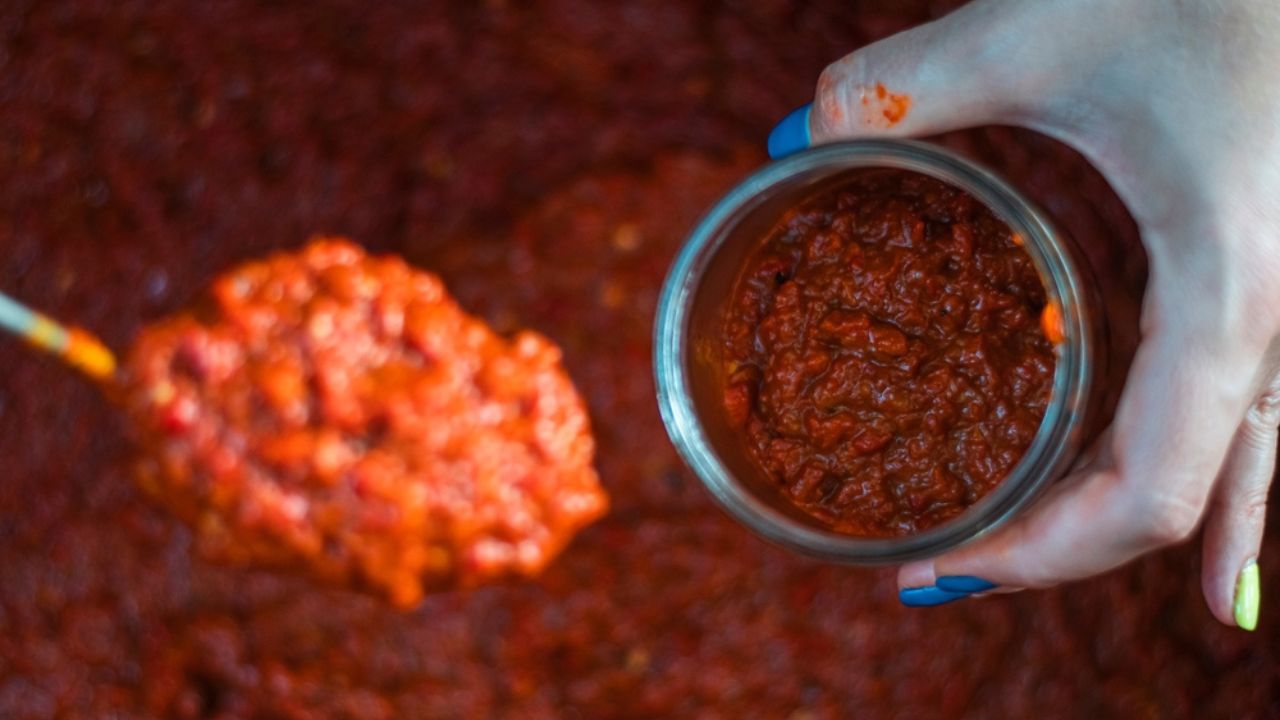 Putting a spoon full of lyutenitsa in a jar. Traditional Bulgarian tomato, eggplant, paprika, pepper sauce paste. High quality photo