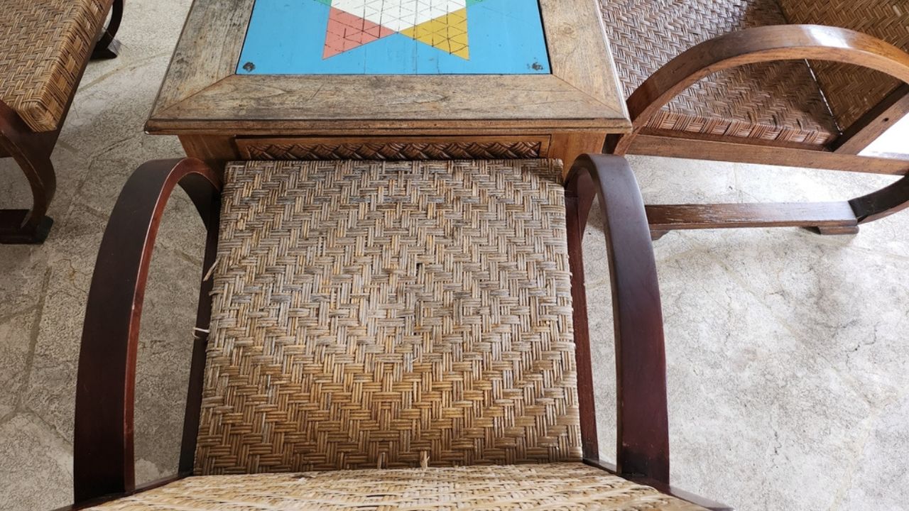 A captivating view of antique wooden chairs with woven rattan seats encircling a game table featuring a vibrant hand-painted game board. Rich textures and colors.