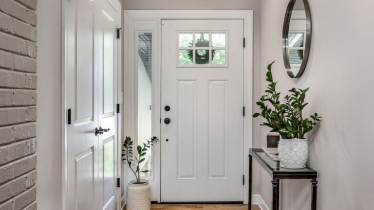 A cozy entryway with brown and brick walls, hardwood flooring, decorations, and a white front door with windows.