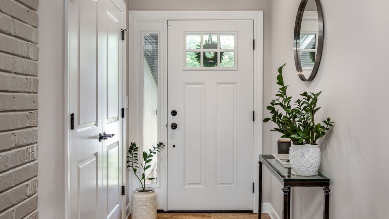 A cozy entryway with brown and brick walls, hardwood flooring, decorations, and a white front door with windows.