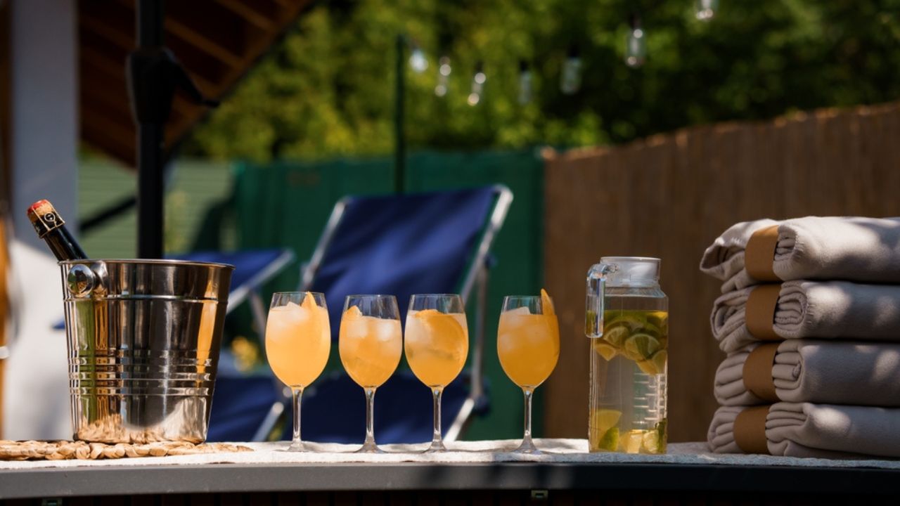 A serene outdoor patio setup featuring a chilled bucket of champagne, refreshing cocktails, neatly folded towels, and comfortable lounge chairs, evoking a warm summer evening mood