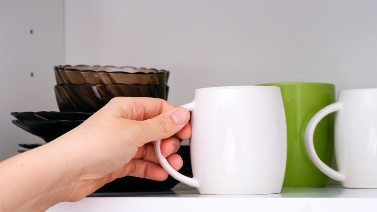 A woman hand taking a white mug from a kitchen shelf.