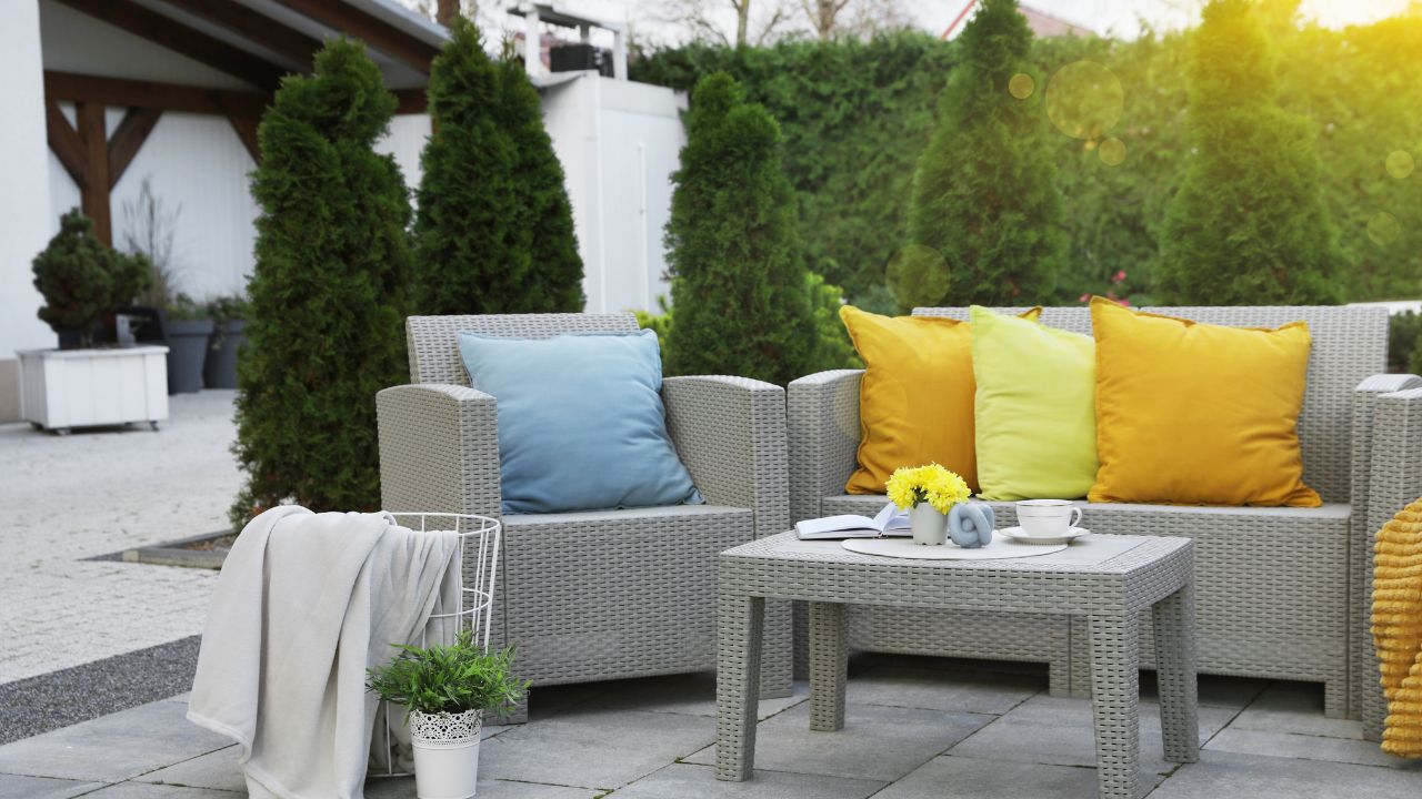 Beautiful rattan garden furniture, soft pillows and different decor elements in backyard