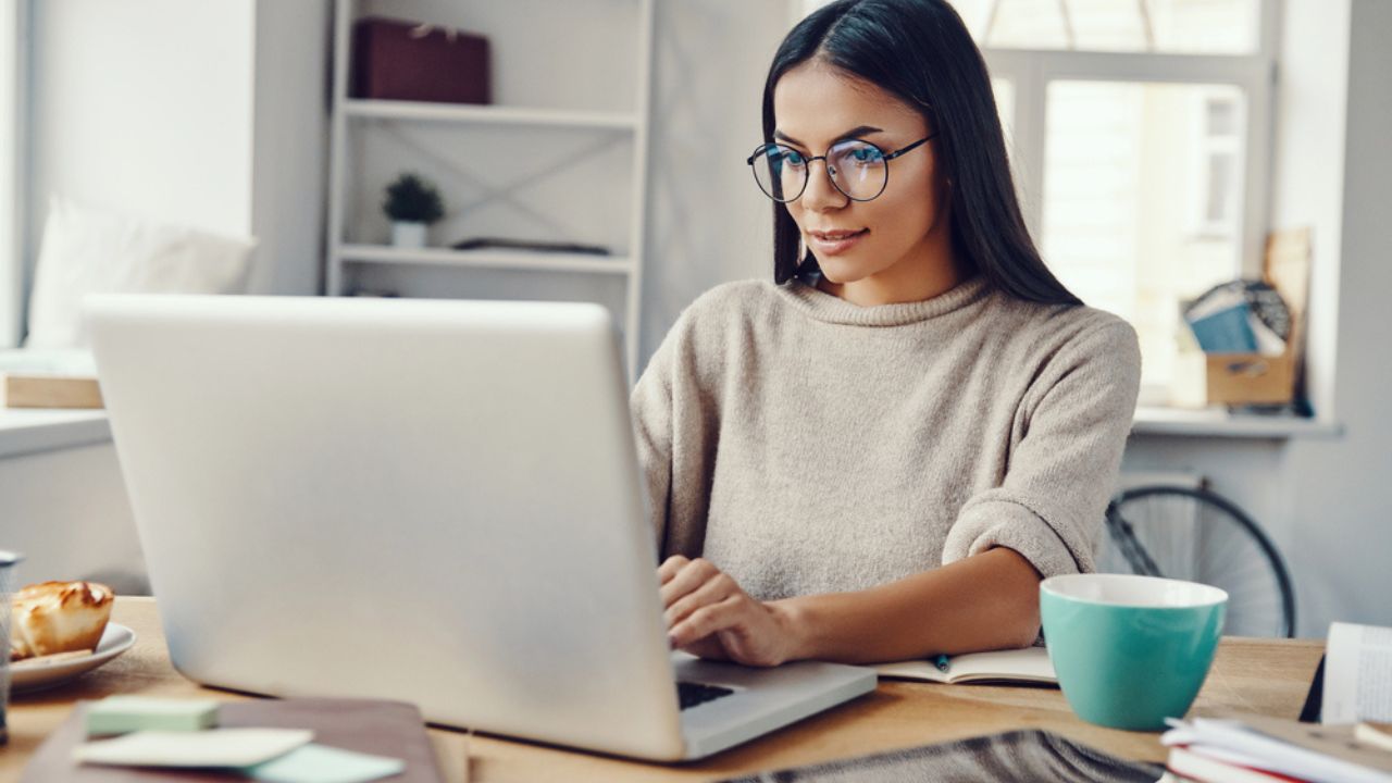 Beautiful young woman in casual clothing using laptop and smiling while working indoors