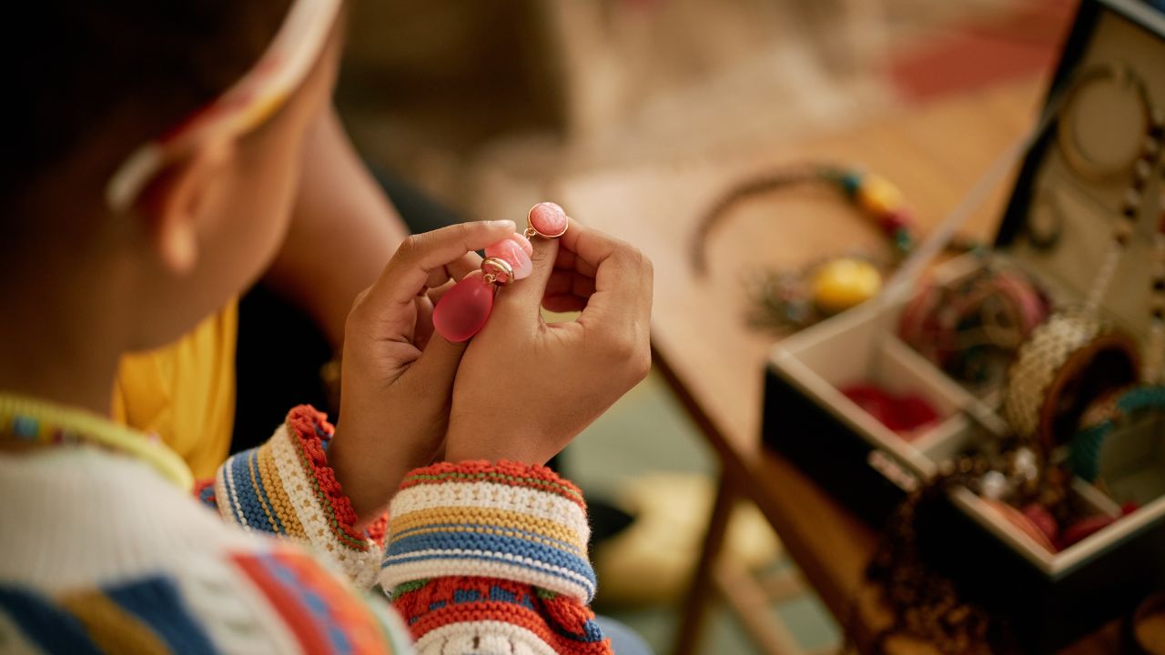 Close up of childs hands holding piece of colorful earrings organizing accessories in jewelry box while bonding with grandmother over heirlooms at home