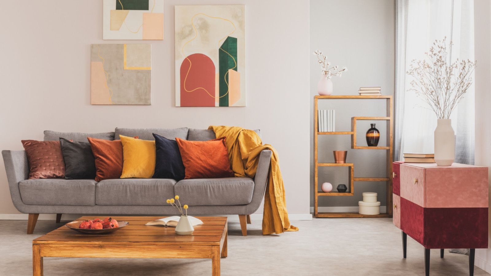 Cozy and atmospheric living room interior with grey couch and pastel pink and burgundy commode